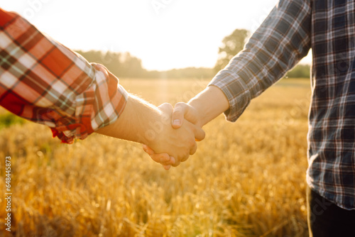 Farmer's handshake against the backdrop of a golden wheat field at sunset. Two farmers stand in a wheat field and seal the deal with a handshake. Agricultural business.