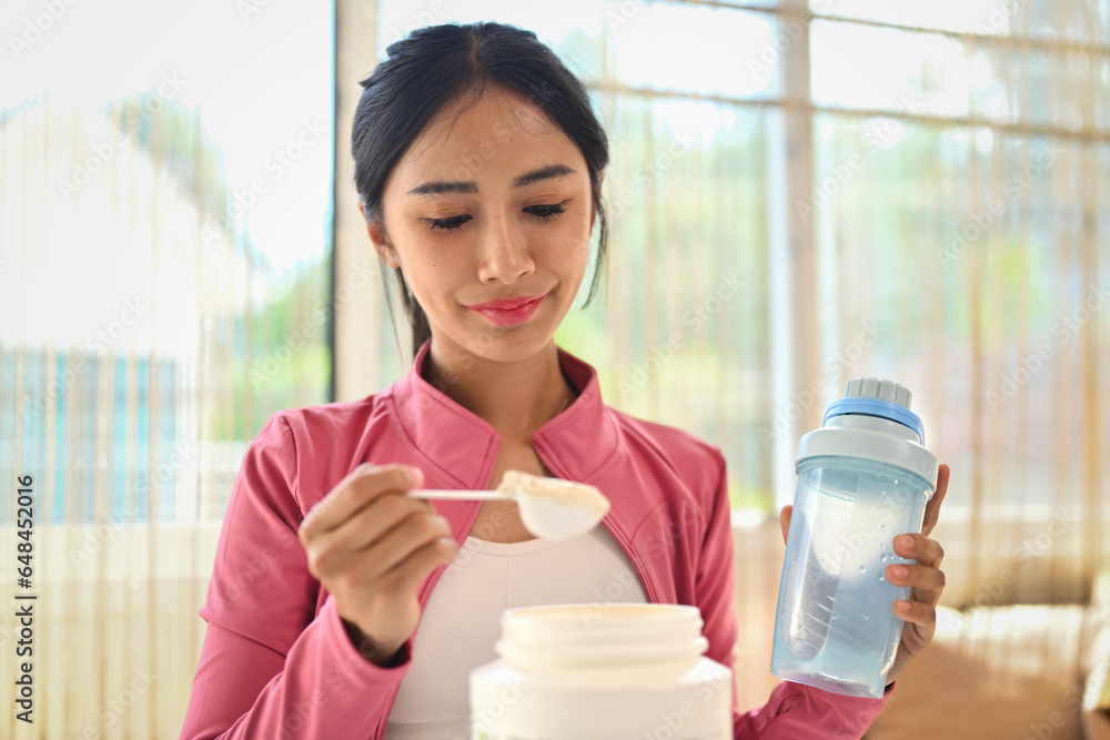 Young sporty woman measuring scoop of whey protein, making replacement food meal after workout Young sporty woman measuring scoop of whey protein, making replacement food meal after workout