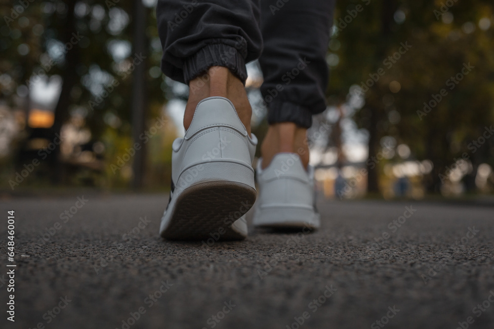 Men's white sneakers on feet in black jeans on the asphalt Men's white sneakers on feet in black jeans on the asphalt