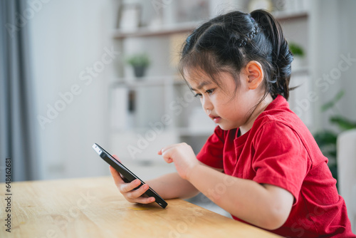 Fotografie Asian child girl looking using and touch mobile phone screen