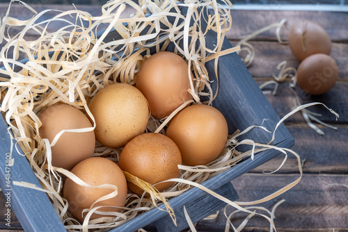 Fresh homemade chicken eggs, brown eggs on straw, eggs in a wooden container filled with straw