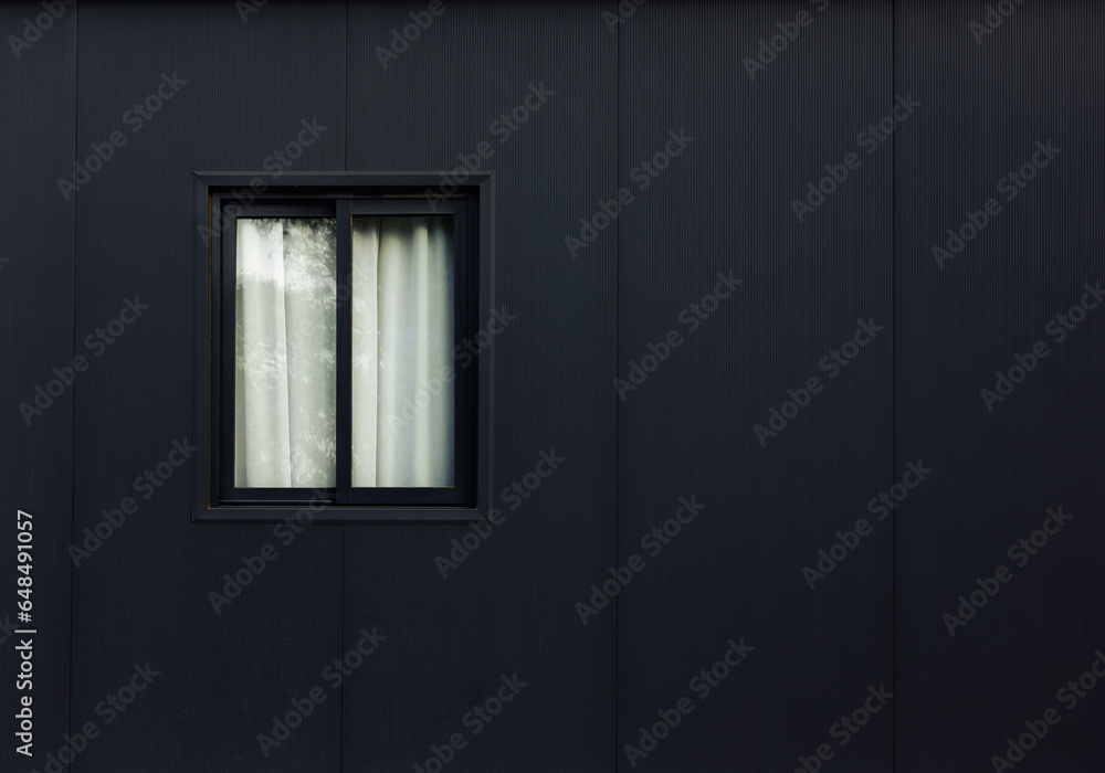 Dark grey facade and illuminated window with cream-colored sheer curtain. Two closed glass panes reveal a glimpse of a soft, cream-colored curtain inside, delicately lit by the evening sun. Dark grey facade and illuminated window with cream-colored sheer curtain. Two closed glass panes reveal a glimpse of a soft, cream-colored curtain inside, delicately lit by the evening sun.