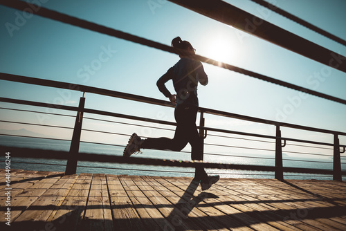Sporty female jogger morning exercise on seaside boardwalk during sunrise