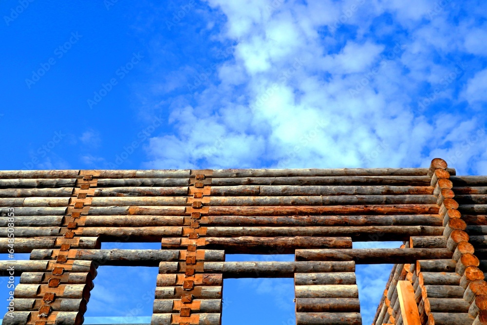 Fragment of a log wooden house, the wall of a house made of logs, against a background of blue sky