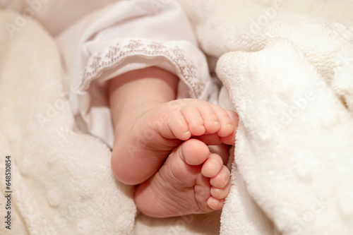 Feet Baby Newborn Barefoot on White Soft  Blanket. Cute Legs of Little Child. Baby Skin Care. Christening in Embroidered Clothing.