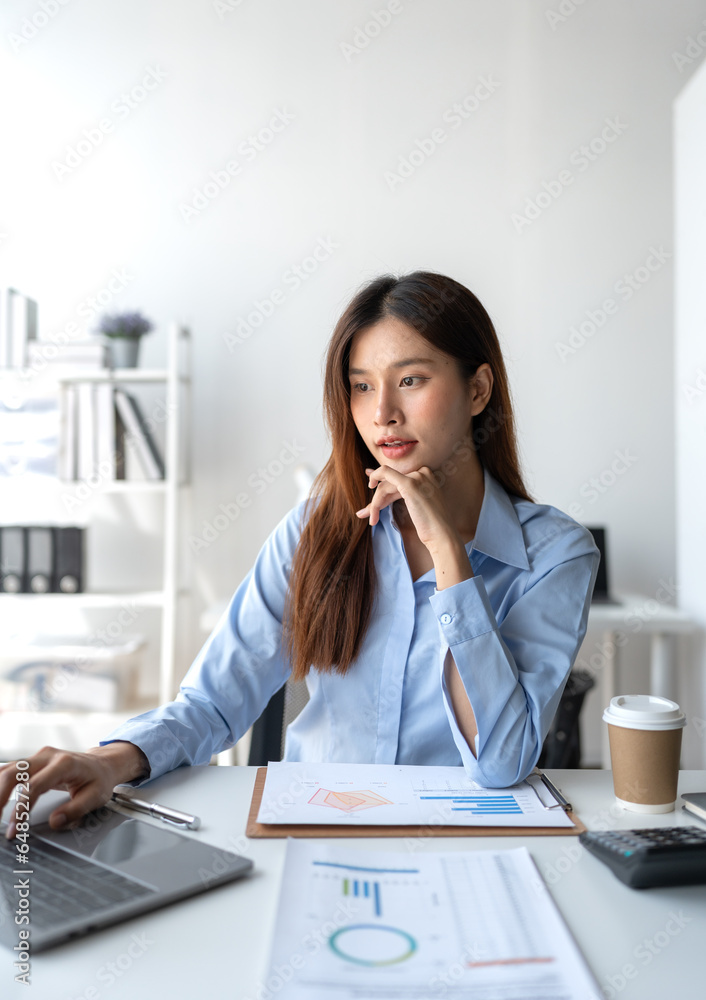 Asian businesswoman sitting and thinking analyze financial reports Business growth using laptop computer and documents, graphs, charts, investment calculators. Office business plan