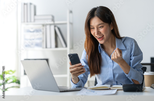 Asian businesswoman raising her hand with a happy expression and looking at her phone The businesswoman was delighted to receive an email informing her of her annual bonus. concept of success