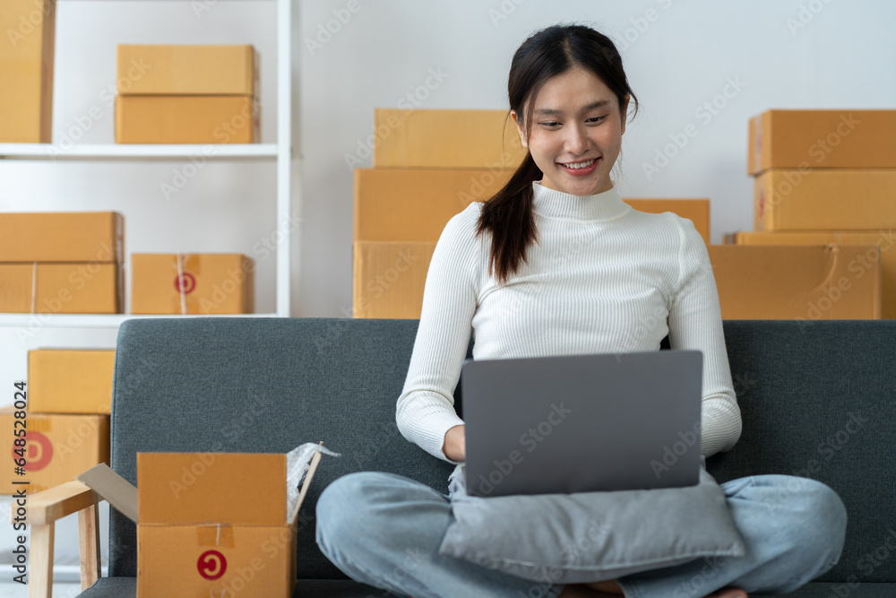 Asian businesswoman taking orders and checking online from laptop and mobile phone to prepare merchandise and deliver to customers in home office. business concept sme e-commerce freelance. Asian businesswoman taking orders and checking online from laptop and mobile phone to prepare merchandise and deliver to customers in home office. business concept sme e-commerce freelance.