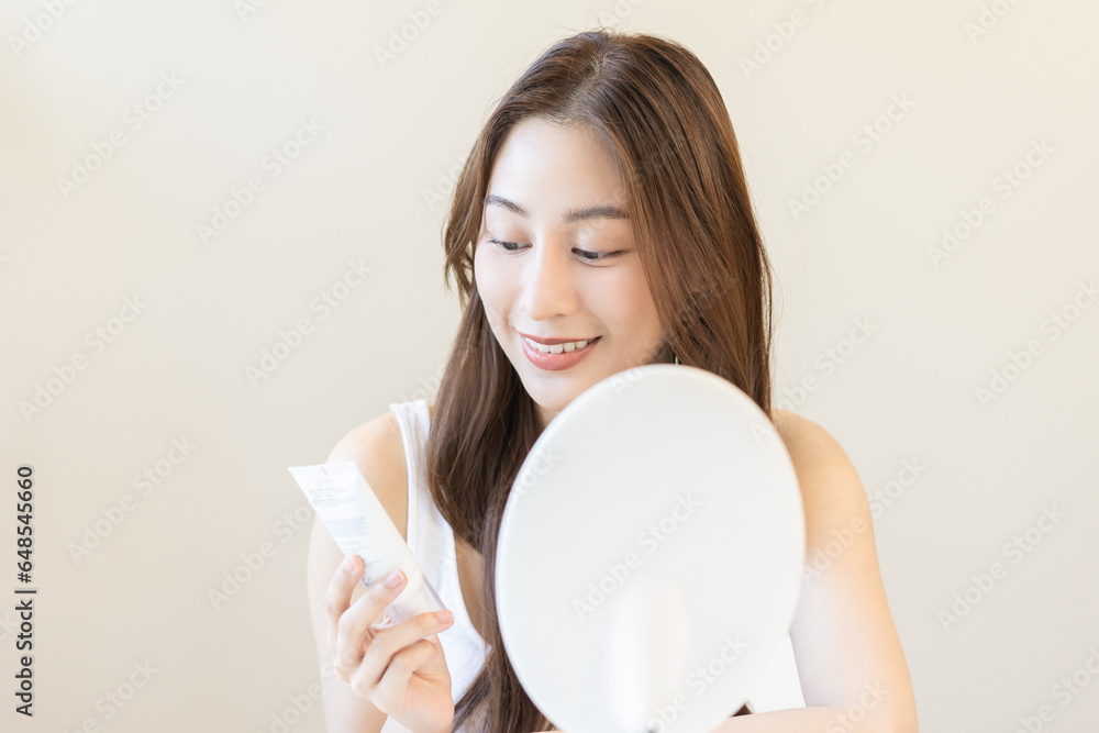 Healthy skin care, smile asian young woman, girl read label to use cream on the tube before applying moisturizer, putting cream treatment on face, makeup routine in the morning at home. Facial Beauty. Healthy skin care, smile asian young woman, girl read label to use cream on the tube before applying moisturizer, putting cream treatment on face, makeup routine in the morning at home. Facial Beauty.