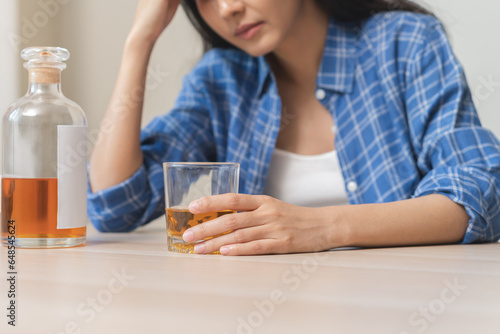 Alcoholism drunk asian young woman hand holding glass of alcohol or whiskey, female sitting alone, drinking on table at home, at night. Treatment of alcohol addiction, suffer abuse problem alcoholism photo