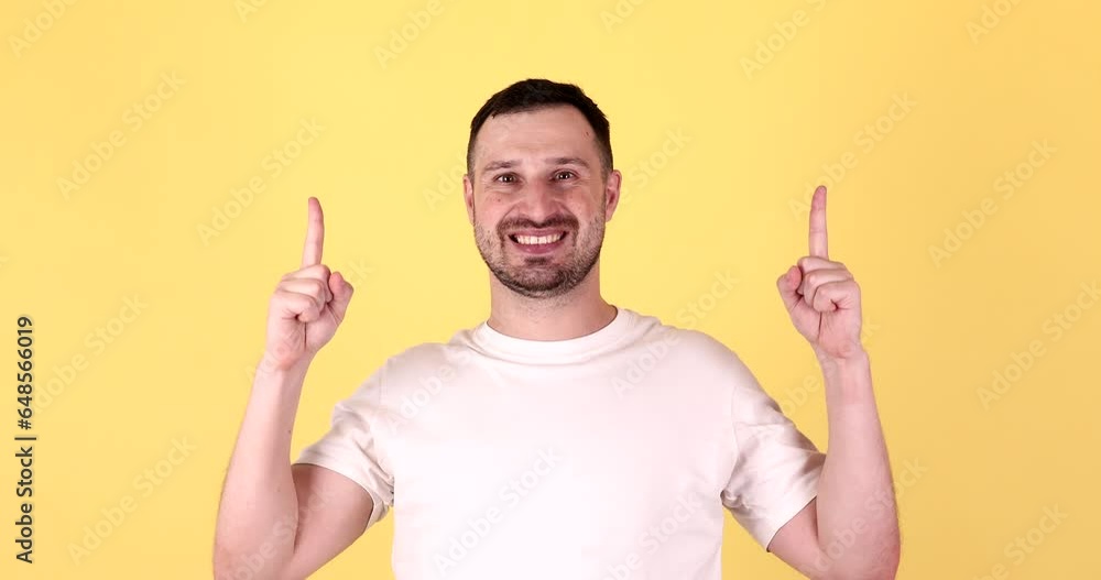 Young man in basic look camera pointing fingers hands up overhead on copy space workspace area isolated on yellow background studio. People lifestyle concept. Young man in basic look camera pointing fingers hands up overhead on copy space workspace area isolated on yellow background studio. People lifestyle concept.