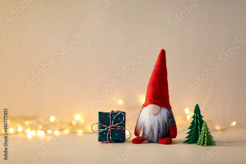 christmas, decoration and winter holidays concept - close up of gnome toy, gift box and fir trees made of green paper on beige background photo