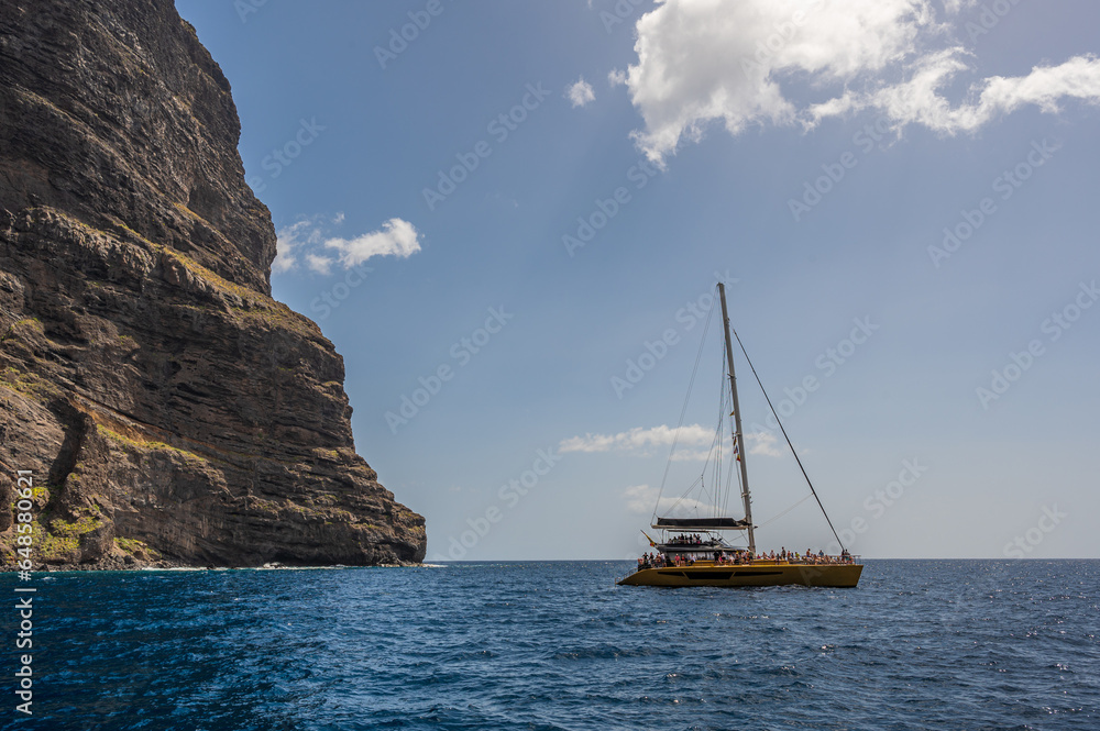 The cliffs of Los Gigantes, Tenerife, rising out of the sea, with a sailing boat on the ocean in front of them The cliffs of Los Gigantes, Tenerife, rising out of the sea, with a sailing boat on the ocean in front of them