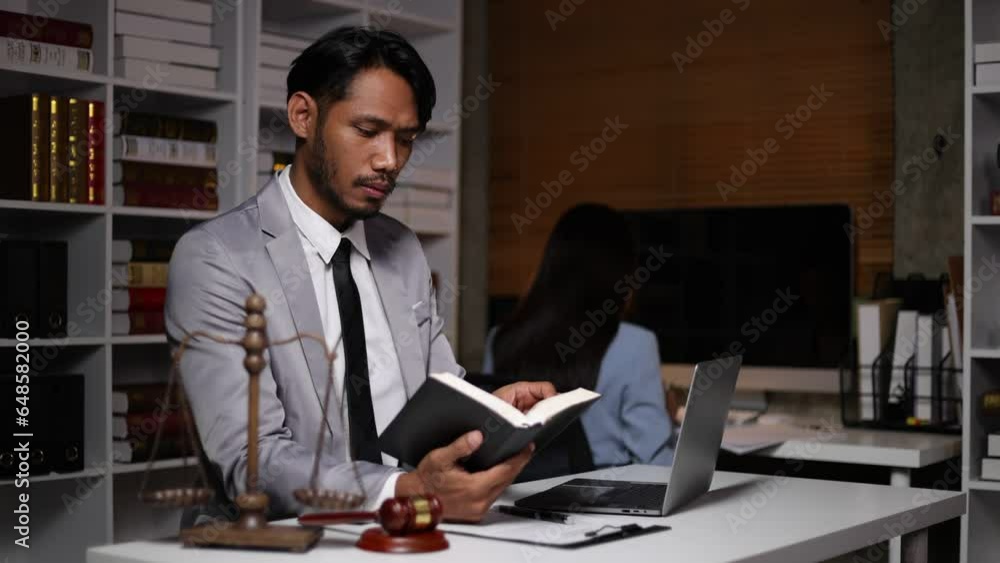 Lawyer reading law book and working on paperwork on laptop at desk in law office. Lawyer reading law book and working on paperwork on laptop at desk in law office.