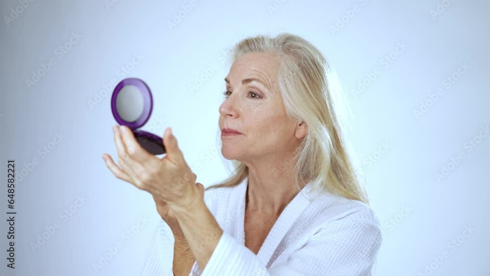 Portrait of mature middle-aged elderly woman wearing robe putting on makeup hygienic look in mirror lipstick applying moisturizing lip balm natural beauty face cosmetics lady white studio background Portrait of mature middle-aged elderly woman wearing robe putting on makeup hygienic look in mirror lipstick applying moisturizing lip balm natural beauty face cosmetics lady white studio background