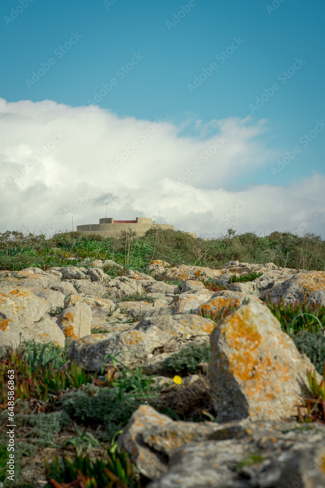 Fototapeta premium na distancia esta um forte marítimo rodeado de pedras e vegetação