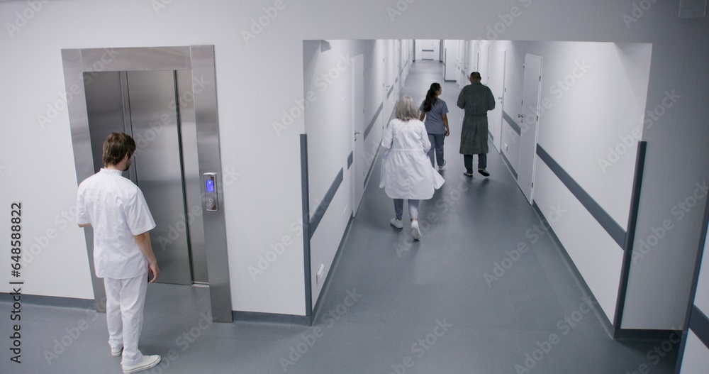 Busy hospital hallway: Diverse doctors, professional medics, nurses and patients walking. Male physician gets into elevator. Medical personnel work in modern clinic or medical facility. High angle.