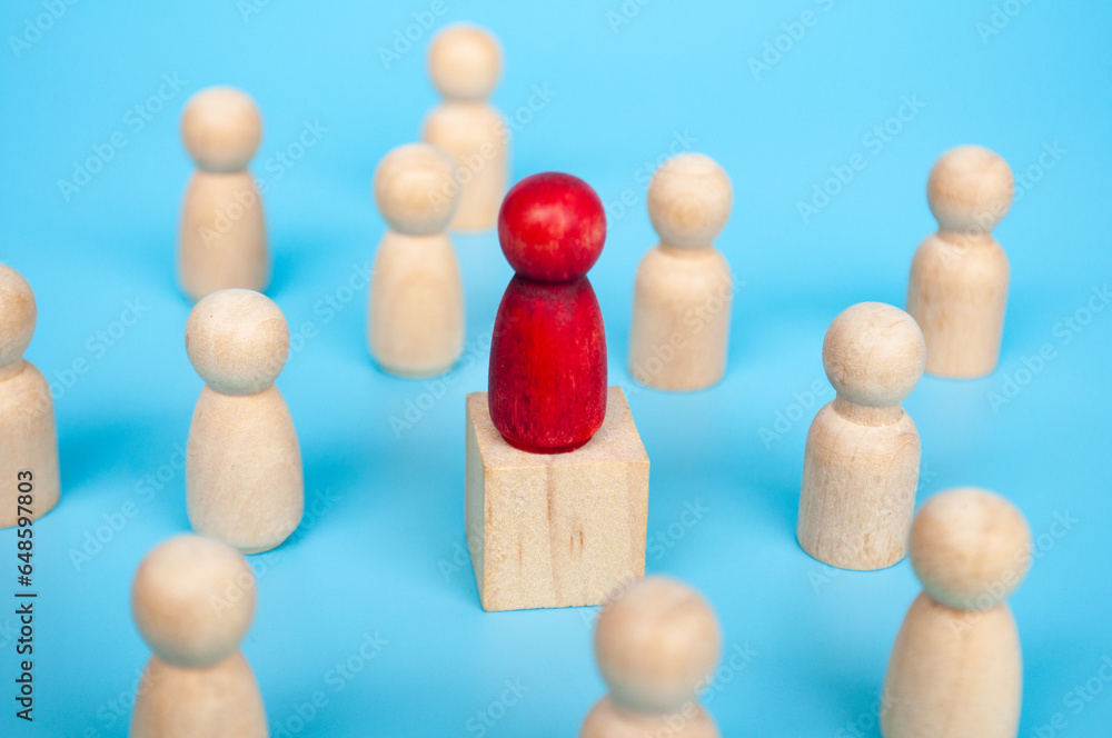 Red figure on top of wooden cube surrounded with other wooden figure. Red figure on top of wooden cube surrounded with other wooden figure.