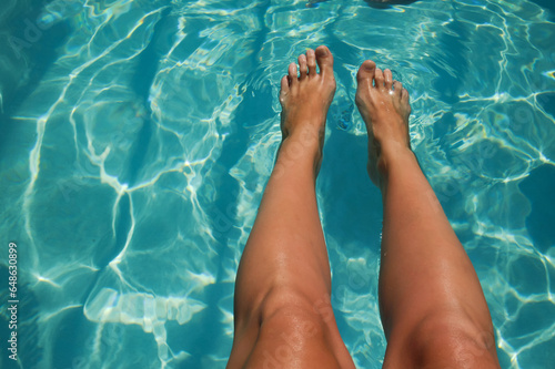tanned legs against the background of clear water in the pool. summer vacation under the sun. background for the design © Alena Mostovich