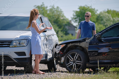 Angry woman and man drivers of heavily damaged vehicles arguing who is guilty in car crash accident on street side. Road safety and insurance concept