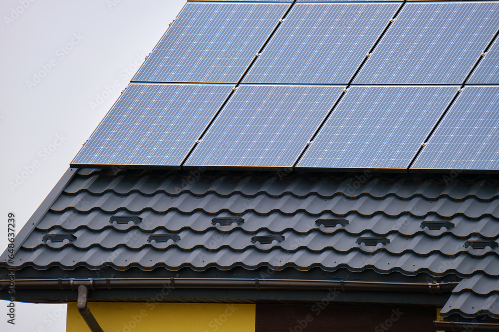 Naklejka premium Private home roof covered with solar photovoltaic panels for generating of clean ecological electric energy in suburban rural town area. Concept of autonomous house