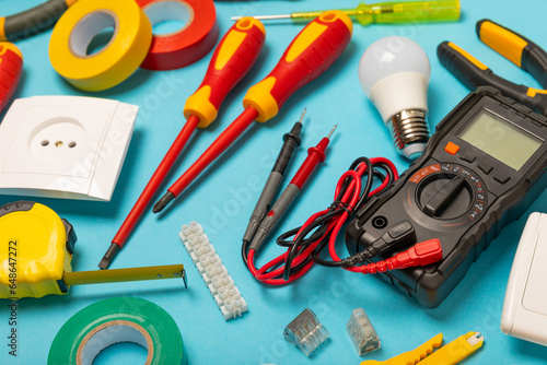 Electrician tools on blue background.Multimeter,construction tape,electrical tape, screwdrivers,pliers,an automatic insulation stripper, socket and LED lamp.Flatley.electrician concept.