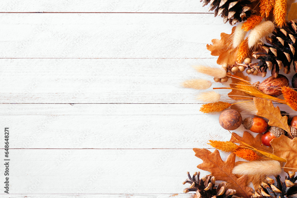 Fototapeta premium Colorful autumn leaves, pine cones, nuts and grasses. Side border over a white wood banner background. Top view with copy space.
