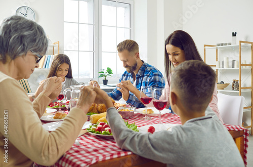 Family praying before meal. Adults and little children celebrating festive event like Thanksgiving Day  sitting all together around dinner table  holding hands  saying prayer  thanking God for food