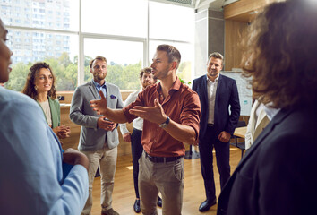 Experienced business coach meeting with a group of people. Young male business trainer or psychologist standing in a circle of men and women, talking about teamwork and giving professional advice