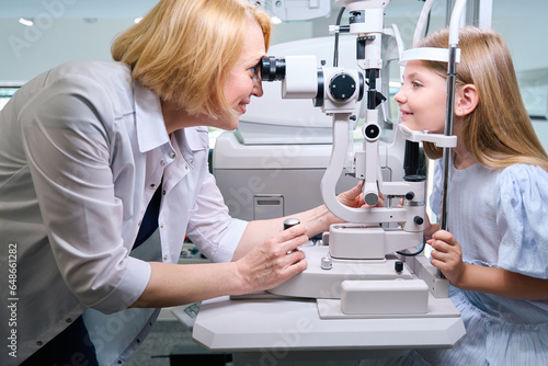 Smiling oculist checking little girl eyesight on modern optical equipment