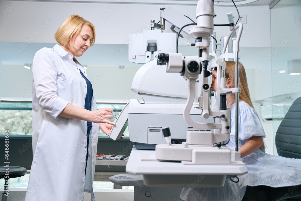 Experienced orthoptist checking little girl vision with autorefractor Experienced orthoptist checking little girl vision with autorefractor