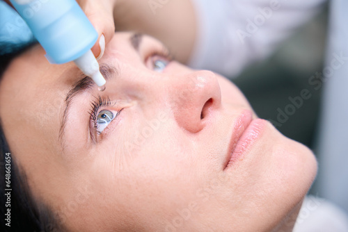 Qualified oculist preparing adult woman for retinal exam