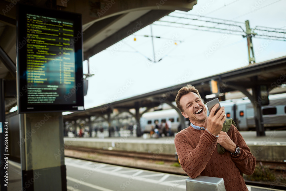 Middle aged businessman using a smartphone while waiting for his train at the train station