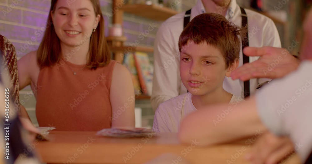 10-year-old child is playing card games with adults without gadgets in urban cafe. Children digital detox. Playtime during technological pause. 10-year-old child is playing card games with adults without gadgets in urban cafe. Children digital detox. Playtime during technological pause.