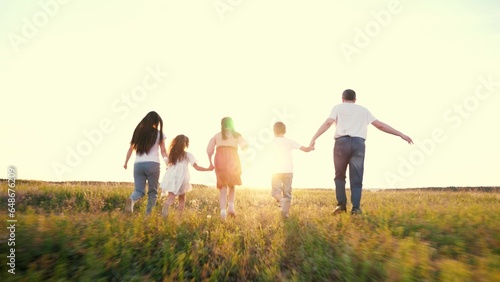 Happy family with little children runs joining hands across green rural meadow