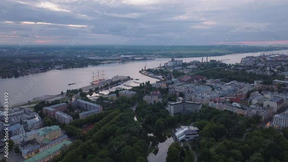 Aerial panoramic view of trees in park, buildings in urban borough and boats in harbour on wide watercourse after sunset. Riga, Latvia Aerial panoramic view of trees in park, buildings in urban borough and boats in harbour on wide watercourse after sunset. Riga, Latvia