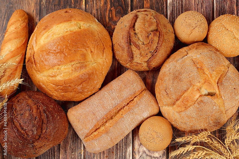 Freshly baked whole grain homemade bread, various varieties of round sourdough bread with crispy crust and ears of rye and wheat on a wooden background, modern baking concept
