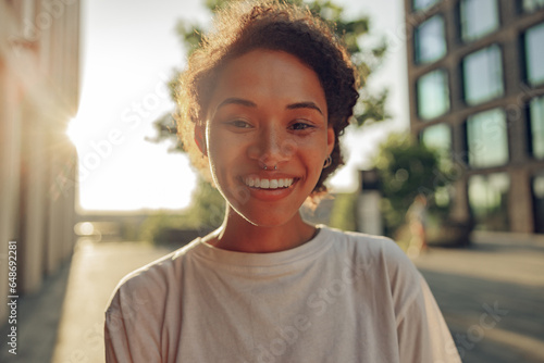 Portrait of pretty smiling young woman standing on modern building background and looks camera