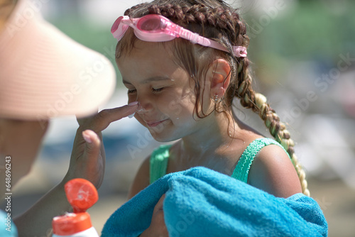 the mother applies sunscreen lotion to the little girl's skin. Skin protection. It is safe to sunbathe on a hot sunny day on the beach. Side view. Close-up.