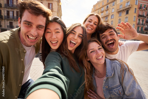 Mobile selfie of group young multi-ethnic beautiful friends having fun together outdoors. Excited people looking at happy camera enjoying sightseeing in city on sunny day. Generation z and vacations.