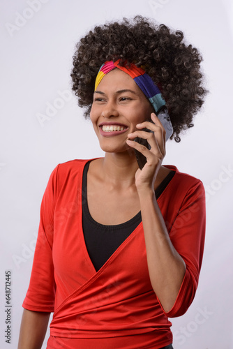 Young black Brazilian woman phoning on cell phone, smiling, wearing red blouse on neutral background photo