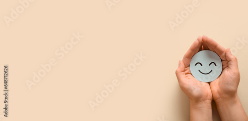 Fototapeta Naklejka Na Ścianę i Meble -  Hands holding paper smiling face on beige background with space for text. World Mental Health Day