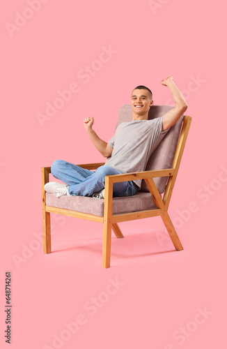 Happy young man sitting on chair against pink background © Pixel-Shot