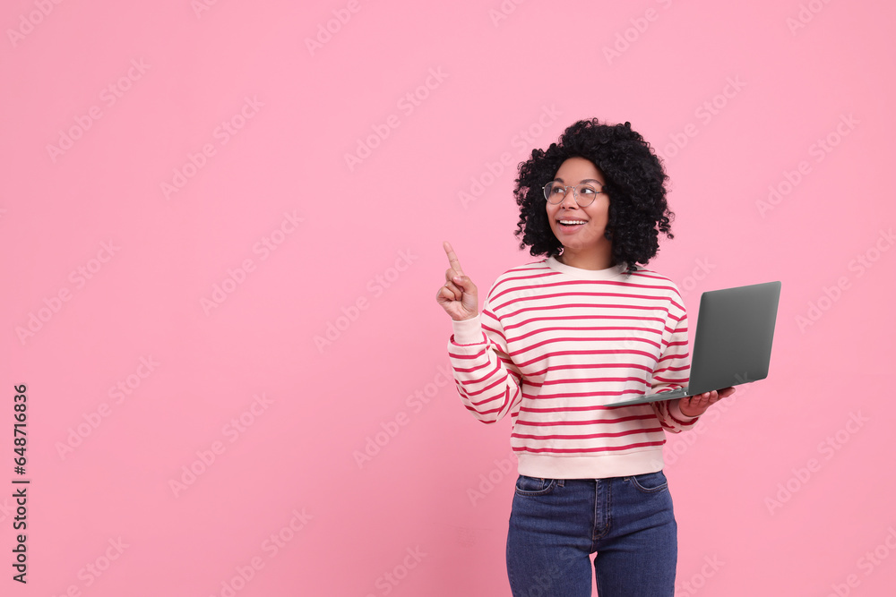 Happy young woman with laptop pointing at something on pink background. Space for text Happy young woman with laptop pointing at something on pink background. Space for text