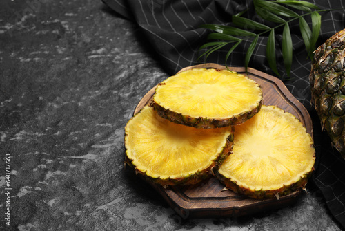 Slices of tasty ripe pineapple on black textured table, space for text