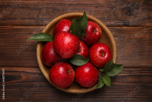 Ripe red apples and green leaves in bowl on wooden table, top view