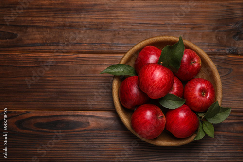 Ripe red apples and green leaves in bowl on wooden table, top view. Space for text