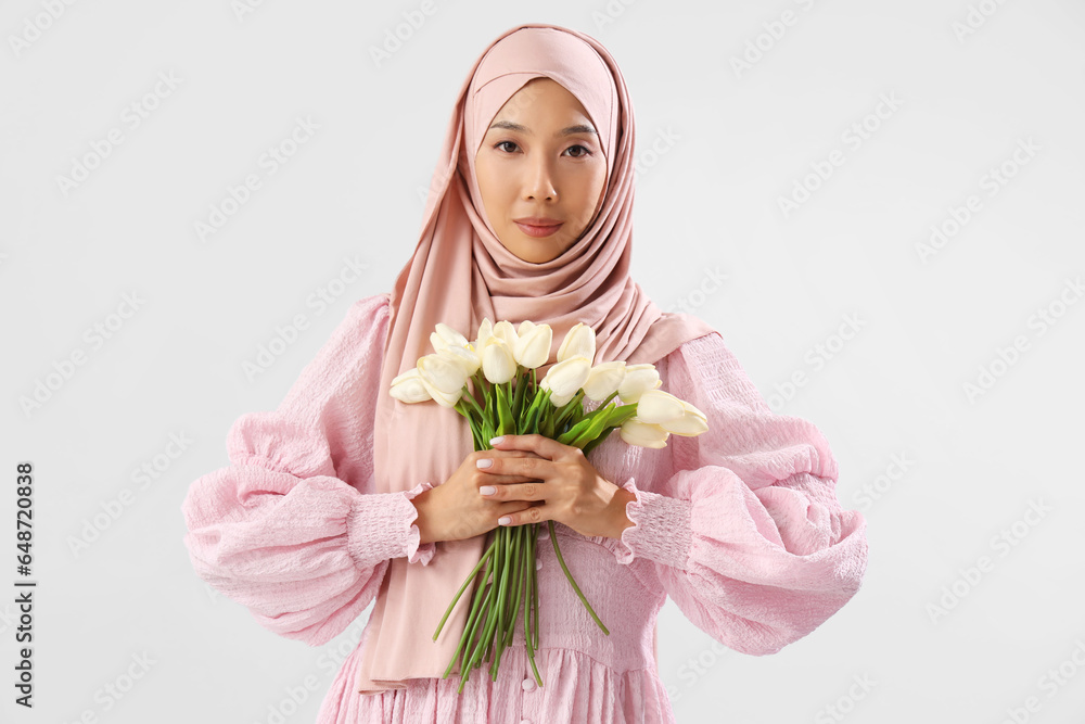 Beautiful young Asian woman in hijab with bouquet of tulips on grey background Beautiful young Asian woman in hijab with bouquet of tulips on grey background