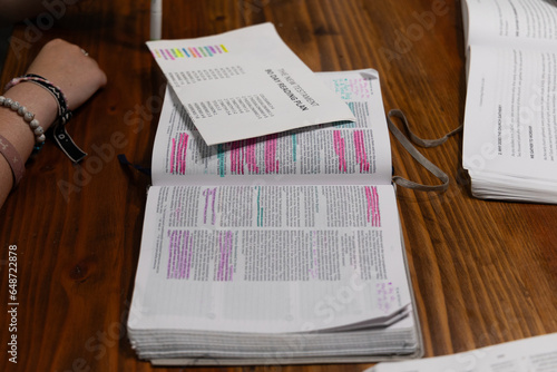 Open Bible laying on table with pink highlighter on pieces of text with Bible reading plan paper on top