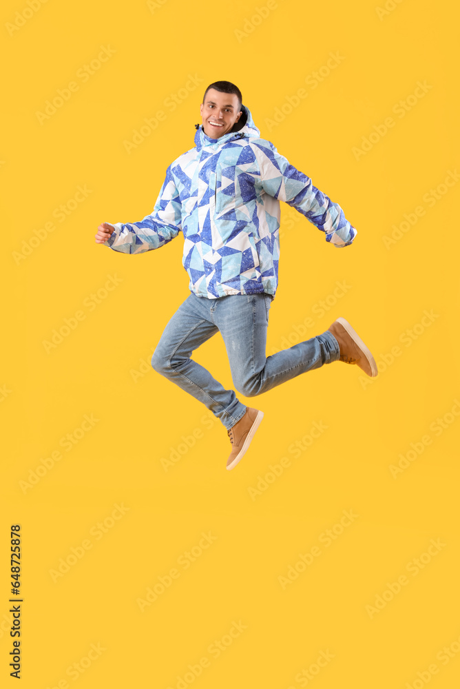 Young man in warm jacket jumping on yellow background